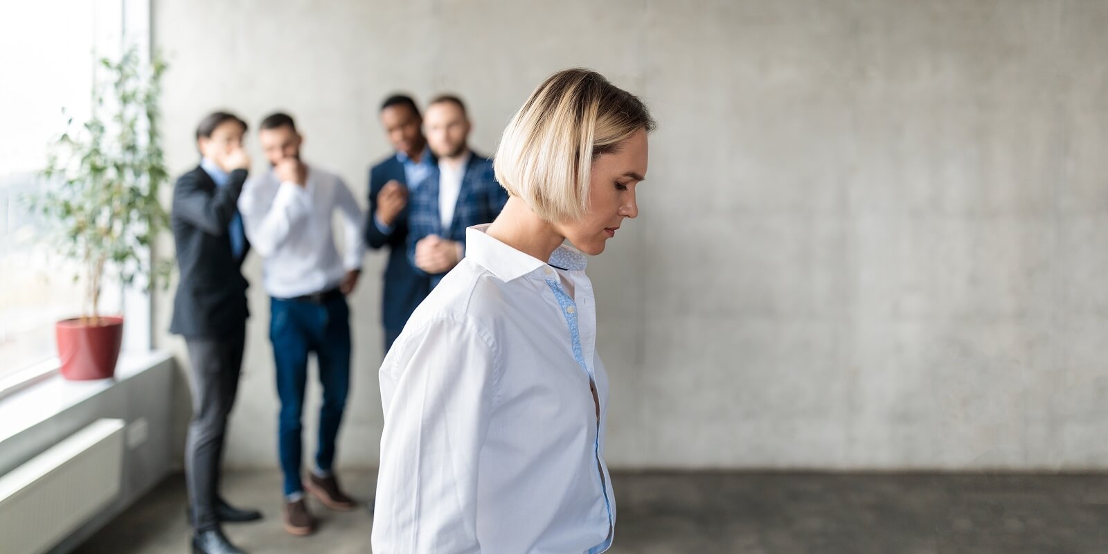 colleagues whispering behind back of unhappy business lady indoors